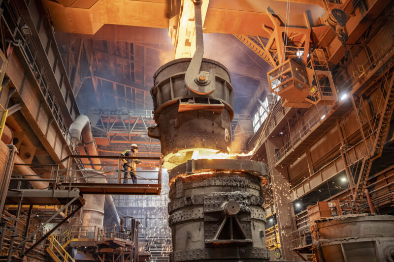 Steelworker starting molten steel pour in steelworks facility.