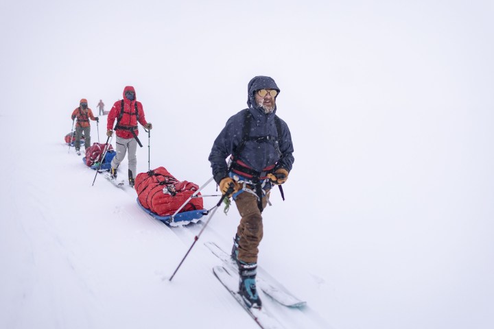 An expedition team walks through the snow while pulling sleds.