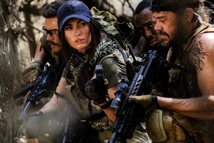 A group of soldiers hold guns and squat next to each other.