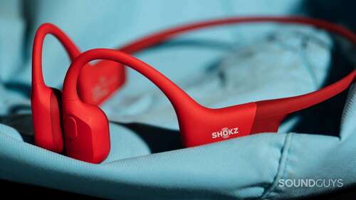 The Shokz OpenRun bone conduction headphones in red on top of a blue surface.