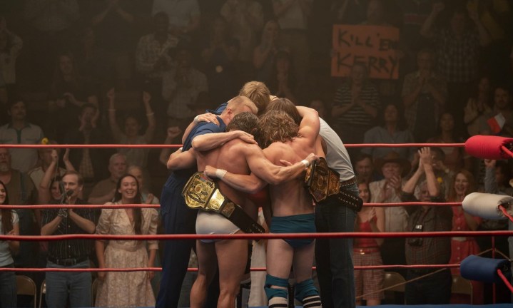 A group of men hug in the center of a wrestling ring.