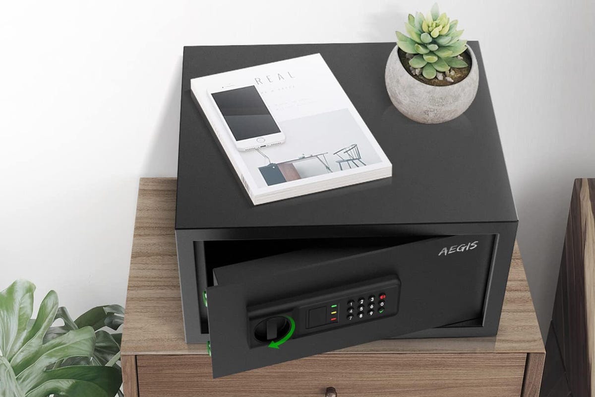 An Aegis safe sits on a wooden cabinet with a stack of papers and potted cactus on top.