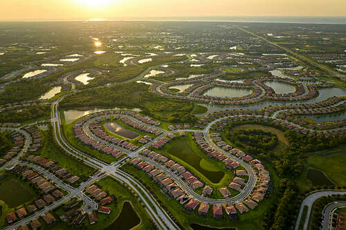 Aerial view of tightly packed homes in Florida closed living clubs with lake water in the middle. Family houses as example of real estate development in american suburbs