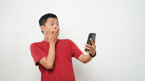 Asian man shocked what he see in the smartphone on isolated grey background