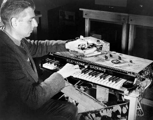 Black and white photo of a man playing a crude-looking keyboard instrument that says Electronic Sackbut.