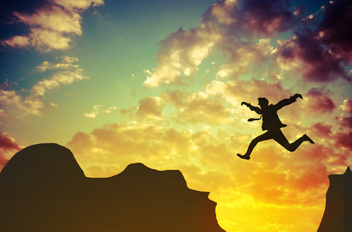 Businessman jumps over rocky mountain.