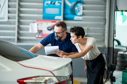 Car Insurance Claims process. Insurance agent explaining damage of car exterior to customer at Auto Repair Center. Business hour 24/7 service coverage. Customer Service, Quality of Service.