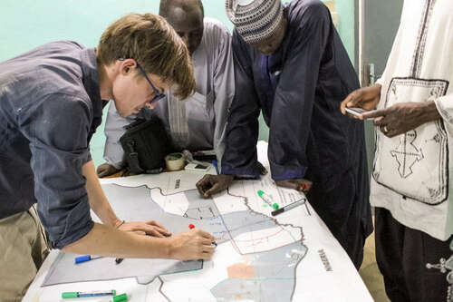 Alex and three other men crowded around a table with a large map of Nigeria