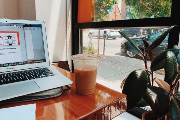 person sitting with computer at coffee shop with iced coffee