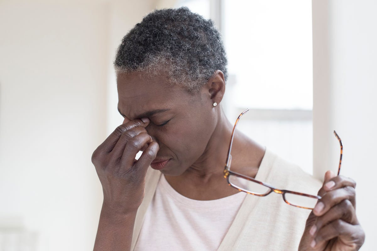 A woman holds her eyes in pain, glasses in hand.