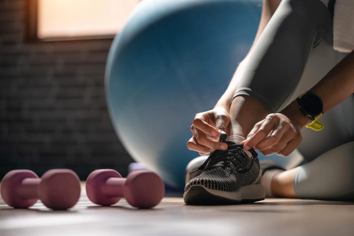 Person tying their shoe. An exercise ball and two small dumbbells are nearby.