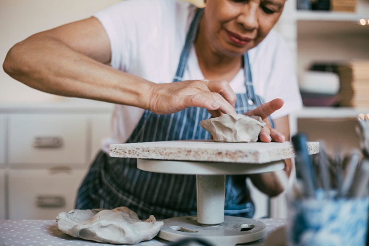 Older woman kneading clay into a bowl.