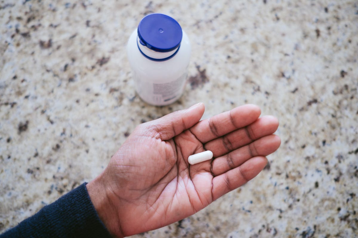 A hand holding a single white vitamin