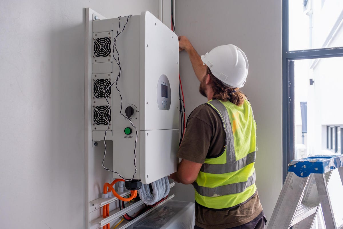 electrician installing a solar inverter on the wall of a house