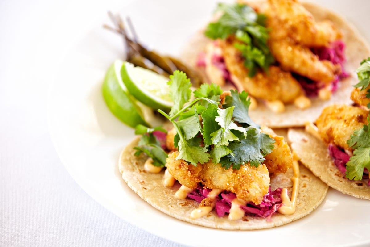 Fish tacos on a plate, with corn tortillas and fresh cilantro.