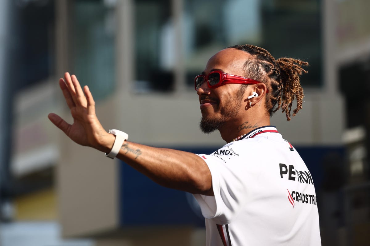 lewis hamilton waves to fans while walking through the paddock