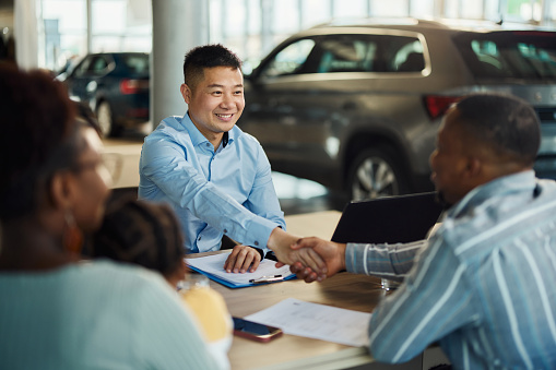 Happy Chinese car salesperson came to an agreement with his customers in a showroom.