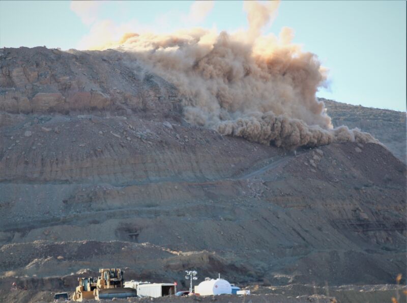 Image of a grey rocky face with part of it exploding.