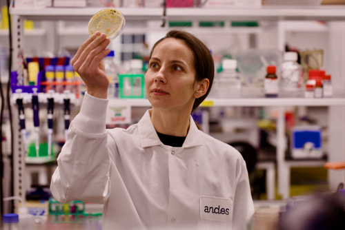 Image of a woman in a lab coat holding a bacterial culture plate