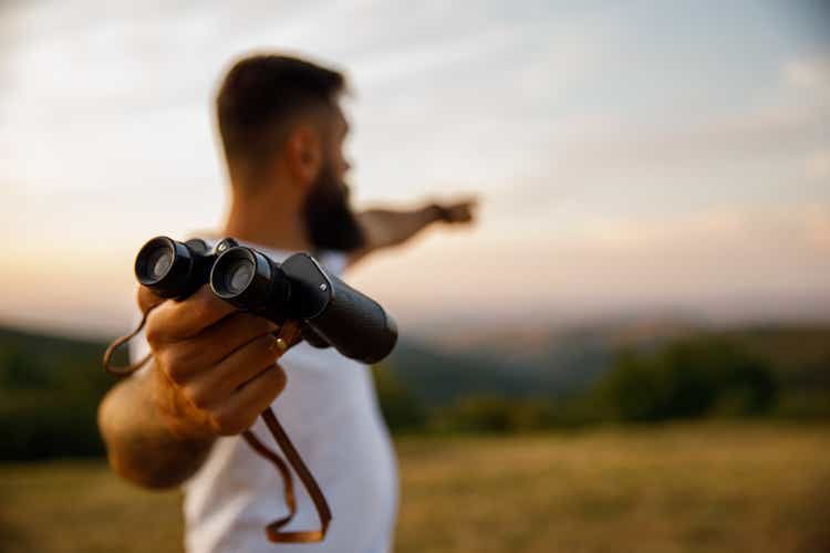 Man giving you binoculars and pointing in the distance to where to look