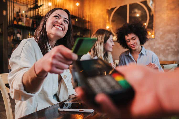 Happy young woman paying bill with a contactless credit card in a restaurant. Female smiling holding a creditcard and giving a payment transaction to the cashier.