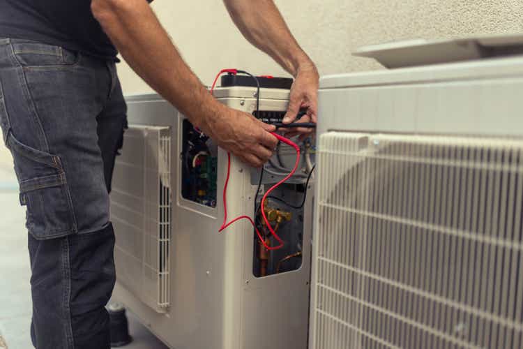 An unrecognizable electrician installs a heat pump in the courtyard of a residential building