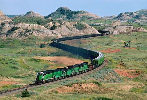 A freight train heads west through the scenic Badlands of North Dakota at Sully Springs on a summer afternoon.