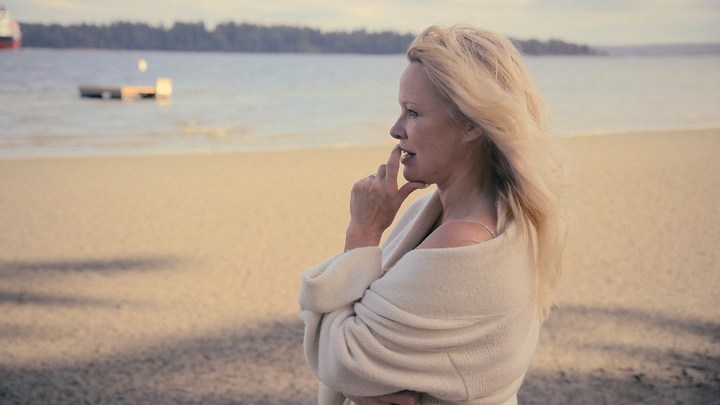 Pamela Anderson standing by the water looking pensive in a scene from Pamela, a love story.