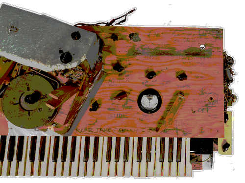 Photo of a musical keyboard instrument showing hand written labels,and assorted electronics.