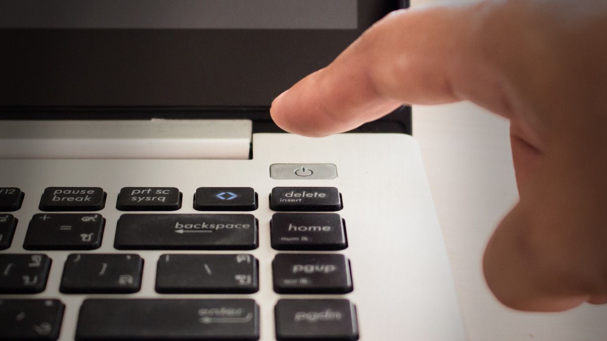 A finger about to press a laptop power button.