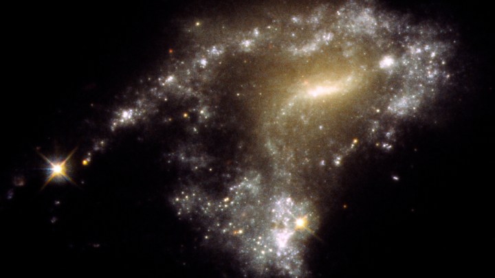 Galaxy AM 1054-325 has been distorted into an S-shape from a normal pancake-like spiral shape by the gravitational pull of a neighboring galaxy, seen in this Hubble Space Telescope image. A consequence of this is that newborn clusters of stars form along a stretched-out tidal tail for thousands of light-years, resembling a string of pearls. They form when knots of gas gravitationally collapse to create about 1 million newborn stars per cluster. 