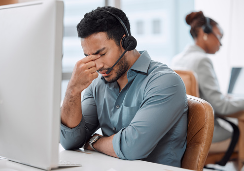 Shot of a young call centre agent looking stressed out while working on a computer in an office