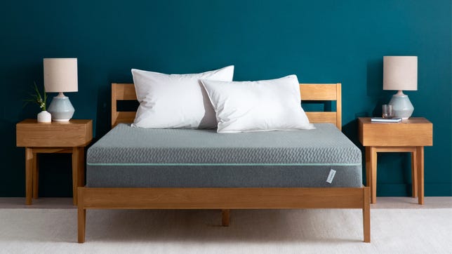 A gray Tuft and Needle Mint mattress staged in a bedroom with blue walls and nightstands