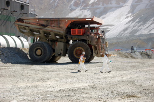 Two miners in white hard hats walk past large mining truck