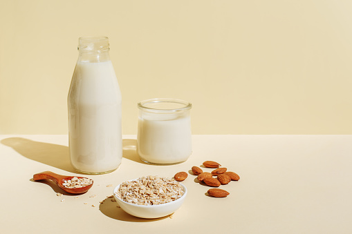 Various organic vegan plant based milk in glasses and glass bottle and ingredients (nuts, oatmeal) on beige background. Non Dairy milk substitute drink, healthy eating. Lactose-free milk in minimal style, copy space.