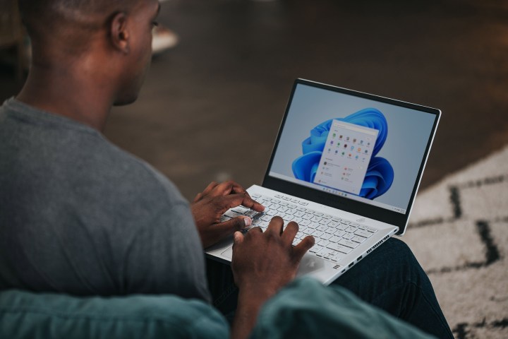 A man sits, using a laptop running the Windows 11 operating system.