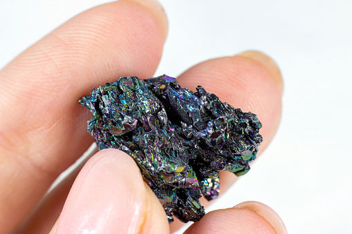 Woman hand holding shiny black Carborundum crystal (Moissanite or Silicon Carbide) on light background close up