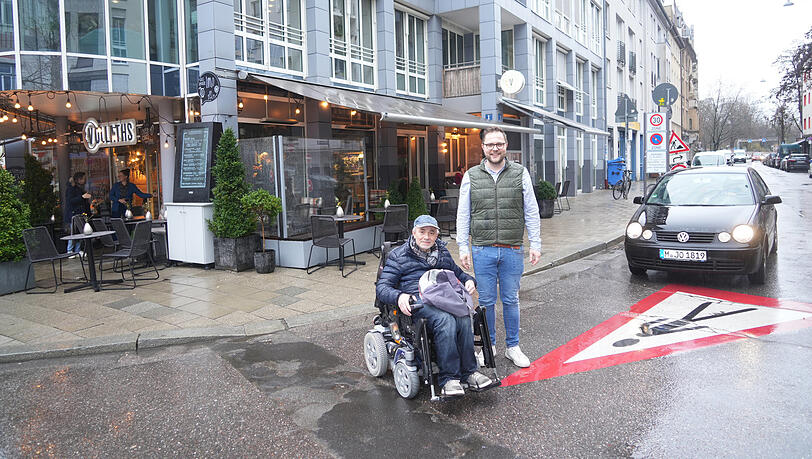 Andreas Vollath (r.) vor seinem Café mit Robert Kaschuba. Für den Rollstuhlfahrer ist diese Ecke zusätzlich schwierig, denn sie ist nicht barrierefrei. Da hilft ihm auch das aufgemalte Warnzeichen auf der Straße nichts.