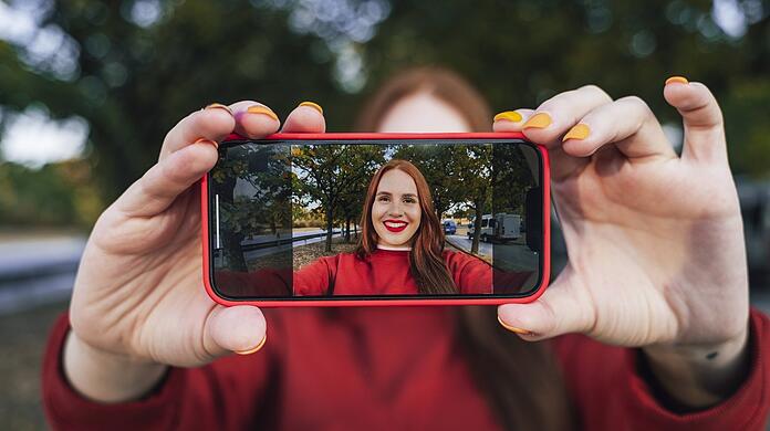 Eine junge Frau filmt sich mit dem Handy selbst. Influencer können Politiker, Sportler, Journalisten, Blogger, YouTuber, Prominente und Schauspieler sein, die mit ihren Internet-Beiträgen durch Werbung Geld verdienen – oft sehr ordentlich.