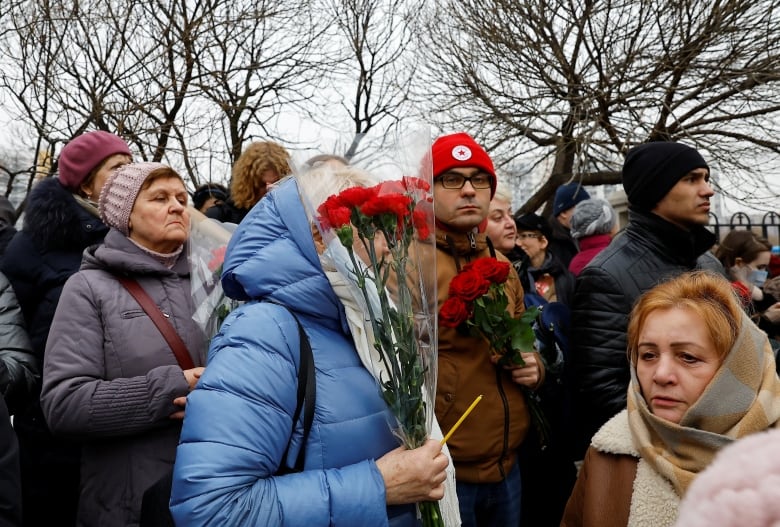 Several people are shown lined up and wearing winter clothing. Some hold flowers.