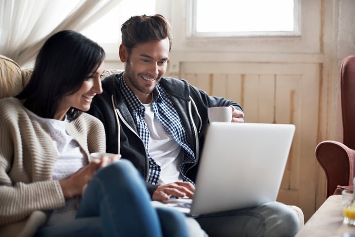 Two people smile while looking at a laptop screen at home.