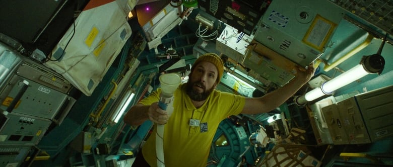 A man wearing a yellow T-shirt floats inside a spaceship.