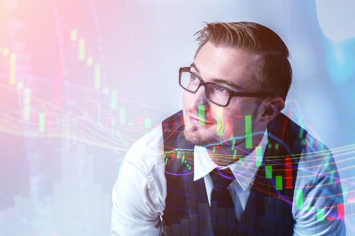 A person wearing business attire smiles with a candlestick chart overlaid on the image.