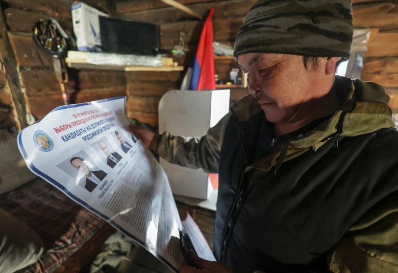 Reindeer herder Arsen Krivoshapkin, 42, looks through a candidates' information broadsheet before casting his ballot during early voting in Russia's presidential election, as members of an electoral commission visit a remote farm in the Sakha Republic, also known as Yakutia, in the northeastern part of Siberia, Russia, February 29, 2024. 