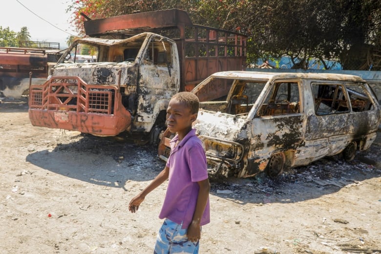 A young child walks by charred cars outside a police station set on fire.