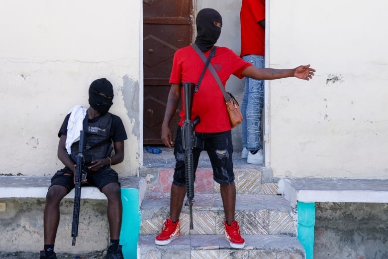 Masked members of a gang stand guard with guns.