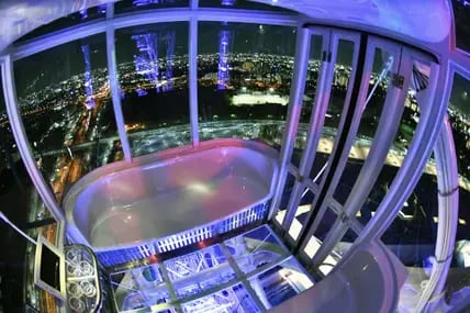 Blick auf eine blau beleuchtete Kabine des Redhorse Osaka Wheel bei Nacht, darunter die erleuchtete City