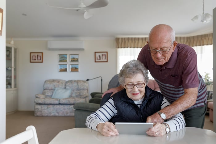 A seated person looks at a tablet while a person stands over them.