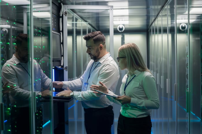 Two people checking on server racks inside of a data center.