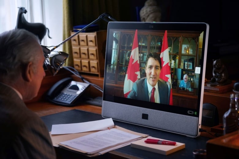 Sitting at a desk, King Charles speaks to Canadian Prime Minister Justin Trudeau, who appears on a large display screen.